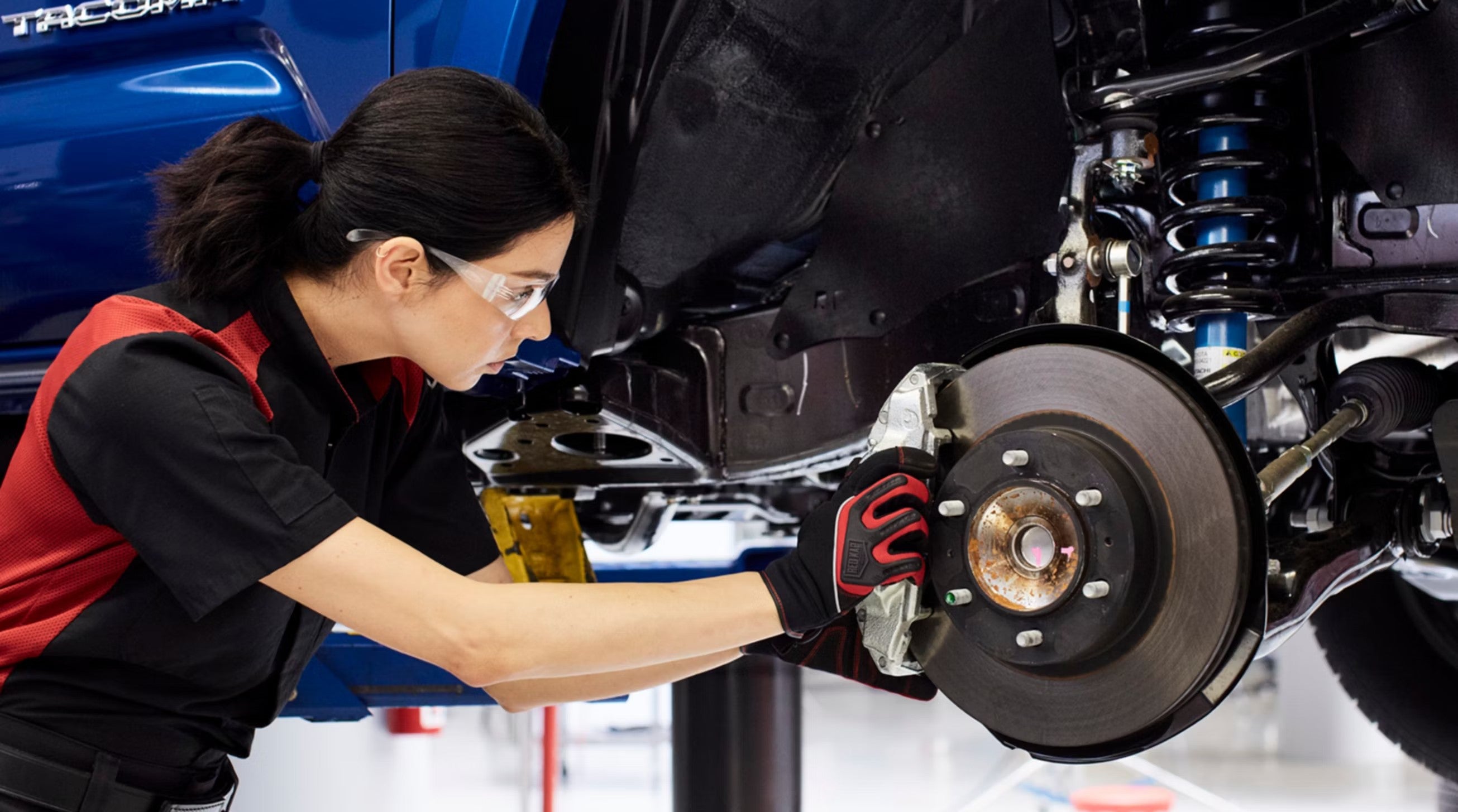 Toyota technician in safety glasses inspecting a brake rotor and caliper on a lifted vehicle